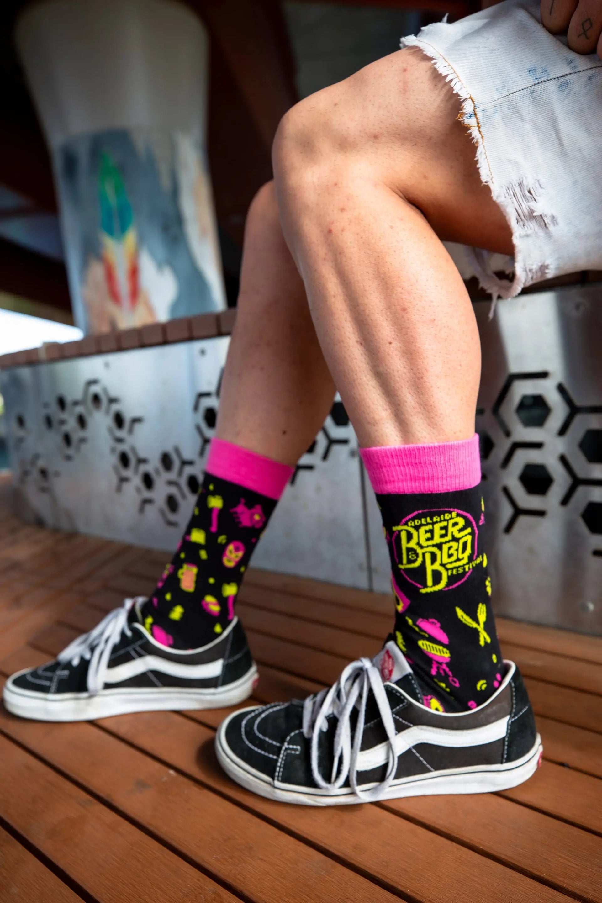 Beer and BBQ Festival socks featuring a  bold and colourful pink, yellow and black design. Model wearing Vans shoes.
