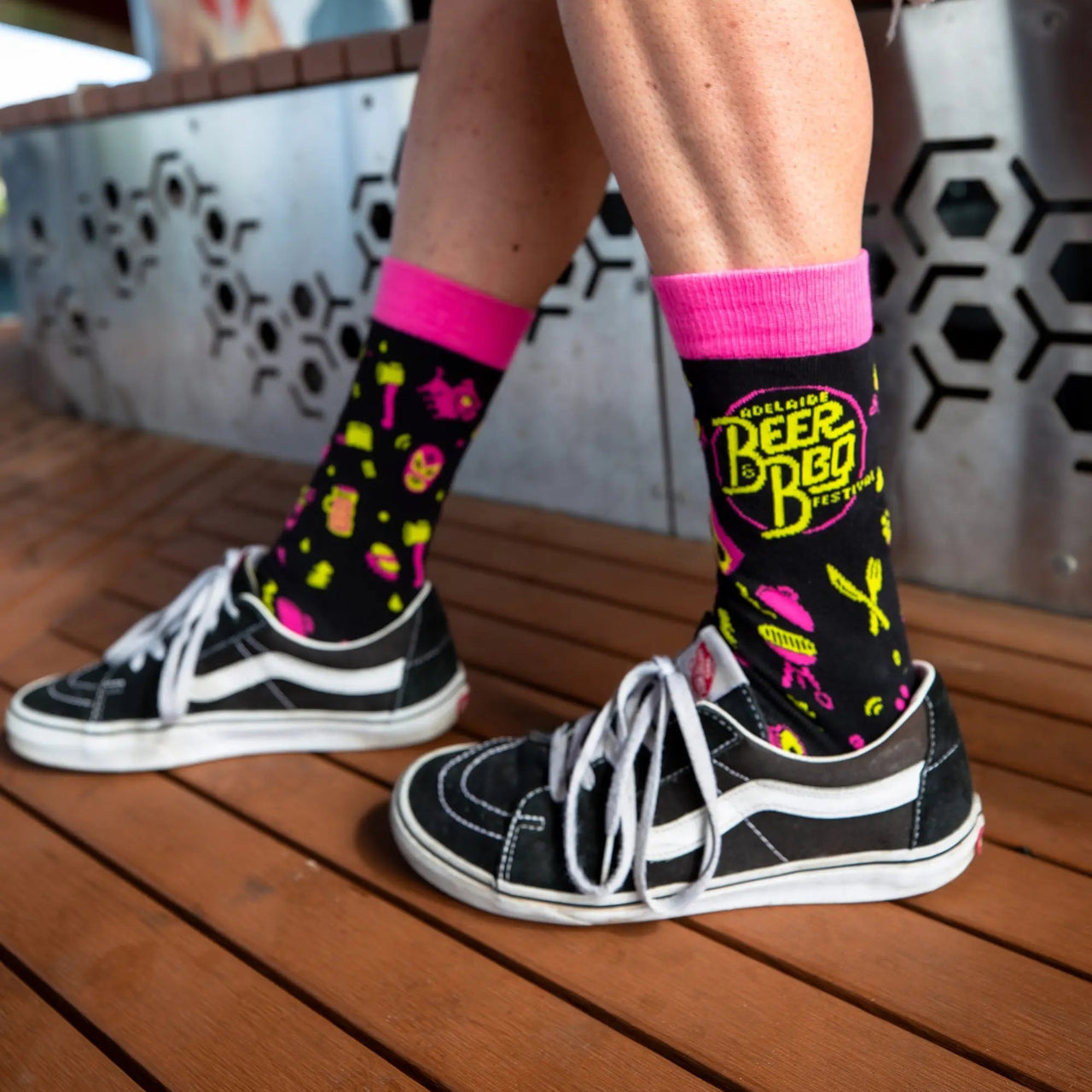 Beer and BBQ Festival socks featuring a  bold and colourful pink, yellow and black design. Model wearing Vans shoes. 