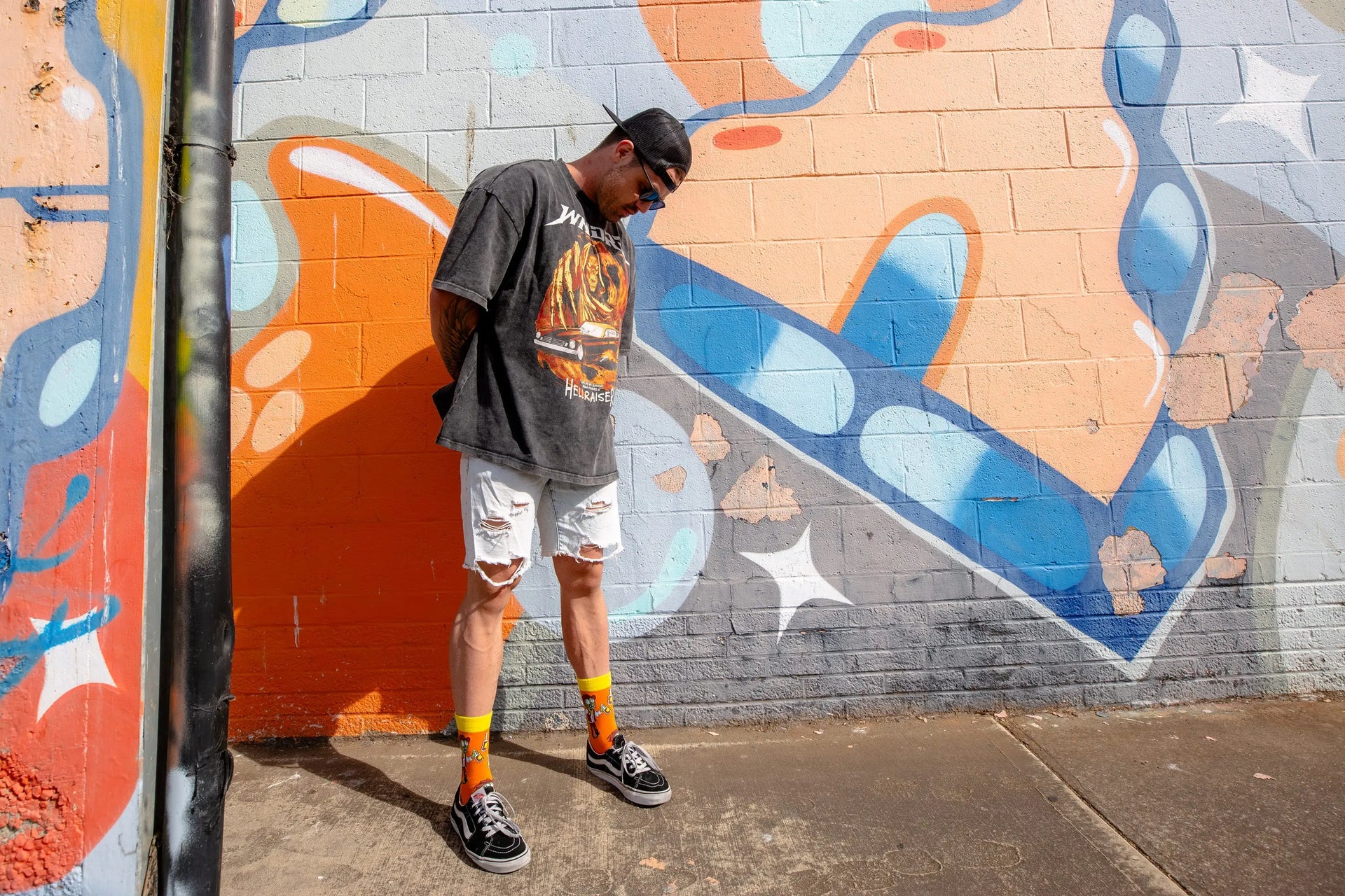 Male model posing next to graffiti wall wearing bright and colourful orange and yellow novelty socks of cowboy zombies drinking moonshine.